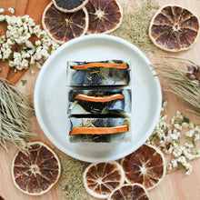 Charger l'image dans la galerie, Savon artisanal naturel Romarin, tangerine et patchouli, Coloré naturellement noir charbon, vert et orange, Avec grains de pavot comme exfoliant, Décoré de tranche d'orange et feuilles, Vue du dessus