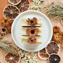 Charger l&#39;image dans la galerie, Savon artisanal naturel Avoine et argousier avec pissenlit, décoré de fleurs et d&#39;agrumes, coloré naturellement beige et orange, vue du dessus
