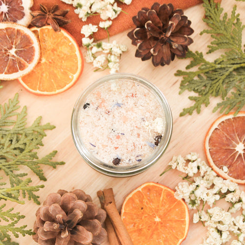 Sels de bain eucalyptus et sapin, faits d'ingrédients naturels et huiles essentielles, décorés de fleurs et feuilles, contenant de verre transparent